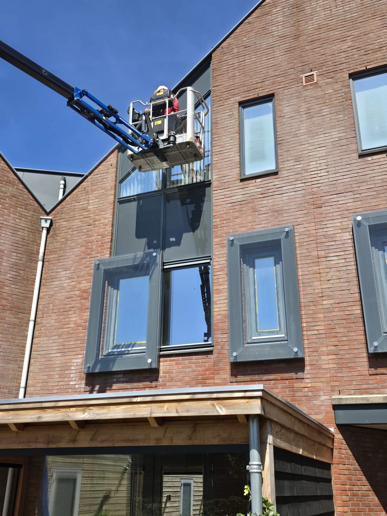 Schilder in hoogwerker die de buitenkozijnen van een gebouw schildert