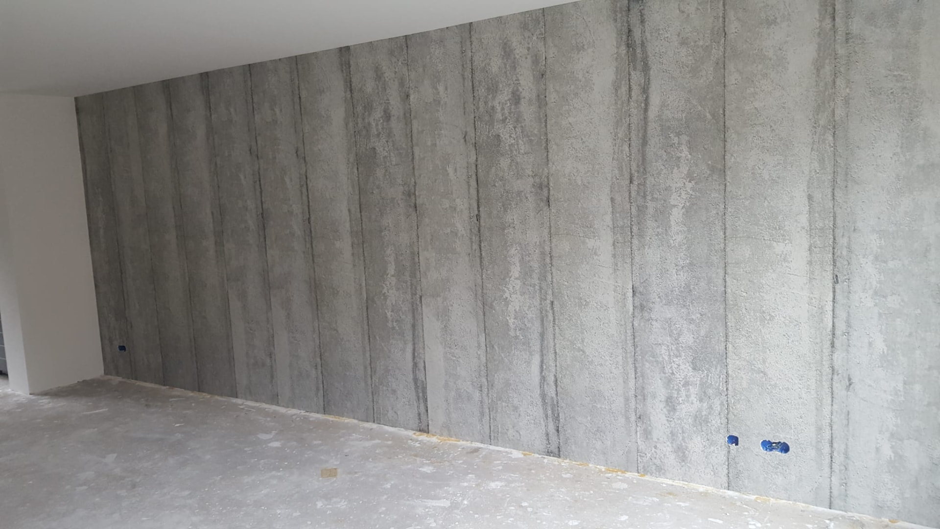 Grote betonlook wand met kimnaden in een woonkamer